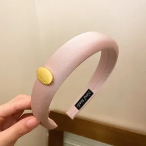 Macro detail of a pink padded sponge headband featuring a gold oval metal decoration.