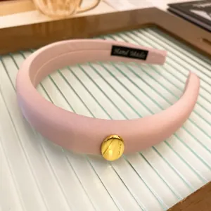 Close-up of pink padded sponge headband featuring a sleek gold oval metal ornament detail