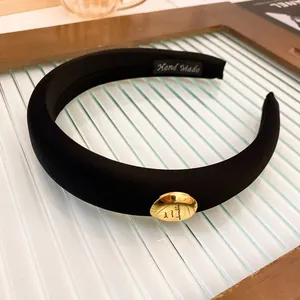 Close-up detail of a black padded sponge headband featuring a stylish gold oval ornament