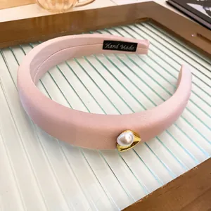 Macro detail of a pink satin sponge headband with a pearl accent and handmade label
