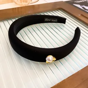 Close-up of black sponge headband featuring a central pearl and gold-toned metal accent.