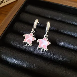 Primo piano di orecchini a stella in resina rosa con cerchi in argento e piccoli strass.