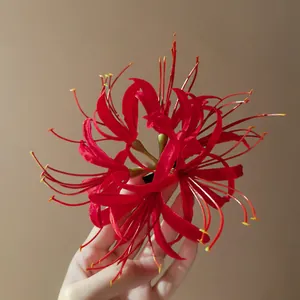 Detailed view of handcrafted red fabric spider lily flower hair clip held against neutral background