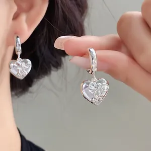 Dettaglio degli orecchini a cuore in argento con fiocco e strass su una modella.