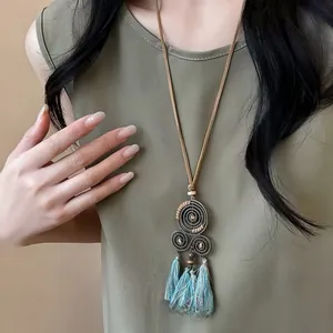 Détail d'un collier ethnique vintage avec des pompons bleus et un pendentif spirale.
