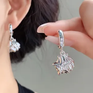 Dettaglio degli orecchini in argento a stella marina e conchiglia con strass brillanti