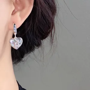 Dettaglio di un orecchino d'argento a forma di cuore con design a fiocco e cristalli.