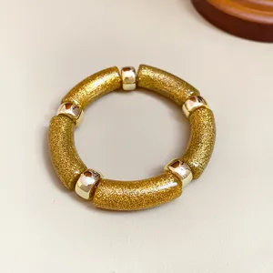 Vista detallada de una pulsera de acrílico con purpurina dorada y cuentas de metal.