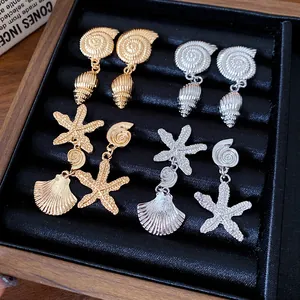 Primer plano de pendientes de estrella de mar y concha en oro y plata con textura.