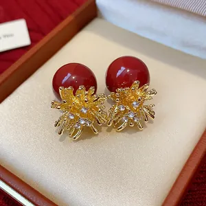 Close-up of red pearl earrings with golden firework rhinestone design in a gift box.
