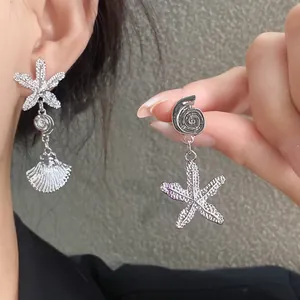 Detalle de pendientes asimétricos plateados con forma de estrella de mar y caracola.