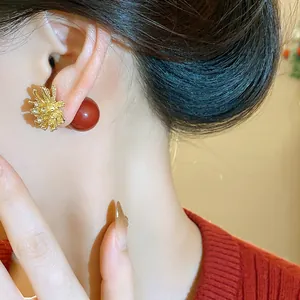 Detailed close-up of elegant gold firework earrings featuring a red pearl and rhinestones