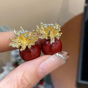 Close-up of elegant red pearl stud earrings with sparkling gold fireworks design detail.