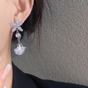 Primer plano de pendientes colgantes de estrella de mar y concha de plata puestos en la oreja