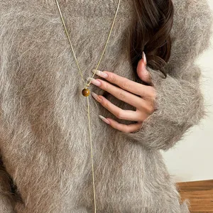 Gold plated drawstring necklace featuring tiger eye stone bead on fuzzy sweater model.