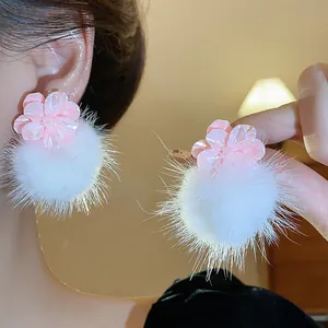 Dettaglio orecchini a fiore in resina rosa con pompon bianchi soffici portati sull'orecchio