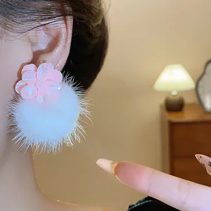 Dettaglio di orecchini a fiore in resina rosa con pompon bianchi, stile invernale trendy.