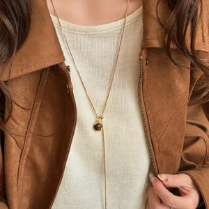Detail view of a gold-plated necklace with tiger eye stone on a brown jacket outfit.