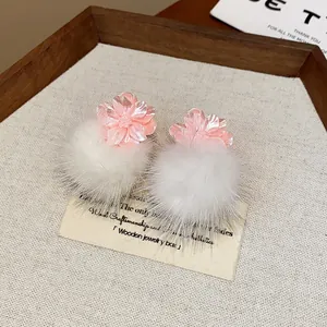 Primo piano di orecchini a lobo con fiore in resina rosa e pompon in pelliccia bianca.