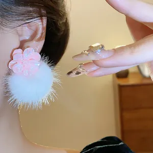 Primo piano di orecchini a fiore in resina rosa con un morbido pompon bianco