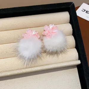 Dettaglio di orecchini a fiore in resina rosa con morbidi pompon di pelliccia bianca soft. (90 chars)