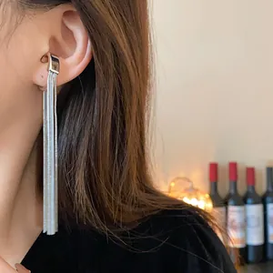 Close-up detail of silver metal tassel ear cuff on model with warm bokeh background