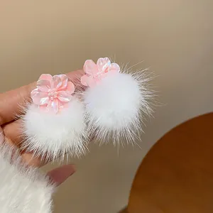 Dettaglio dei dolci orecchini a lobo a fiore in resina rosa con pompon in pelliccia bianca.