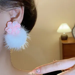 Primo piano di orecchini a bottone con fiori in resina rosa e pompon bianchi su modella.
