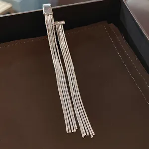 Detailed view of silver metal tassel ear bone clips on a brown textured background