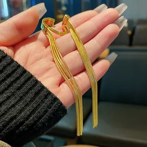 Detail shot of a minimalist gold-colored metal tassel ear cuff held by a hand