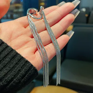 Detailed view of a minimalist silver metal tassel ear cuff held in hand.