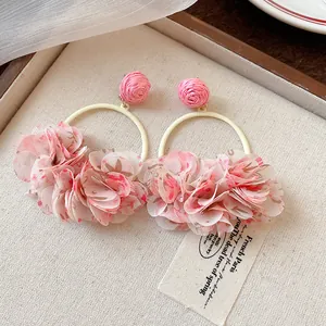 Close-up of pink fabric petal hoop earrings with woven ball detail on a beige background