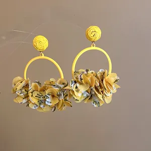 Macro detail of yellow fabric petal hoop earrings on a transparent display stand