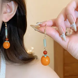 Detailed view of Chinese style persimmon resin drop earrings with enamel flower caps.