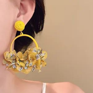 Macro shot of yellow fabric floral petal hoop earrings worn by a model.