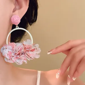Detail view of oversized pink fabric petal hoop earrings worn by a model in a close-up shot