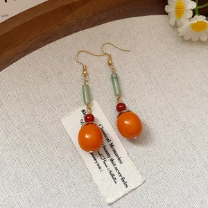 Close-up of vintage style persimmon drop earrings with green beads on linen background