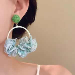 Close-up of large hoop earrings with green woven stud and blue fabric petals on a model.