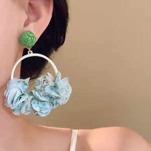 Close-up of elegant hoop earrings with light blue fabric petals and green woven stud