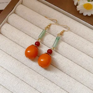 Close-up detail of handmade persimmon-shaped resin drop earrings inside a beige jewelry box
