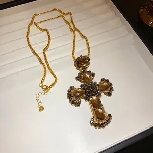 Vue rapprochée d'un pendentif croix baroque avec pierres ambre et cristaux noirs.