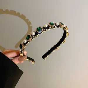 Detailed macro shot of luxury emerald green crystal and pearl headband with gold trim.