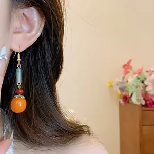Detail view of orange resin persimmon tassel earring with delicate enamel petals.