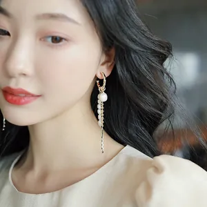 Close-up detail of an elegant C-shaped hoop earring featuring pearls and long chain tassels