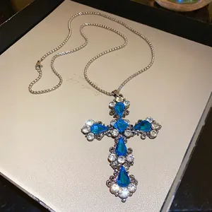 Détail d'un pendentif en forme de croix orné de strass bleus et blancs en gouttes.