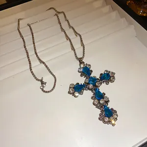 Détail d'un collier pendentif croix en strass bleu étincelant sur un plateau de présentation