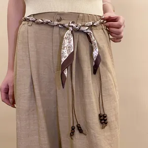 Close-up detail of a woven silk scarf belt featuring decorative wooden beads on waist