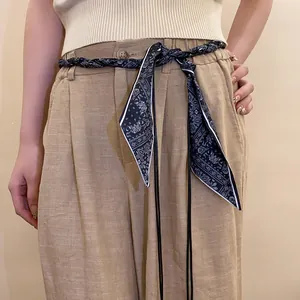 Detail view of a woven silk scarf belt with navy paisley pattern worn on tan pants