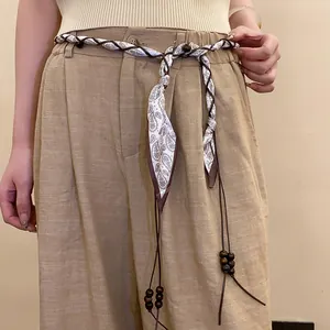 Detailed view of a braided silk scarf belt with wooden beads and paisley pattern