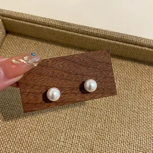 Detail of round white pearl stud earrings on a dark wooden display block